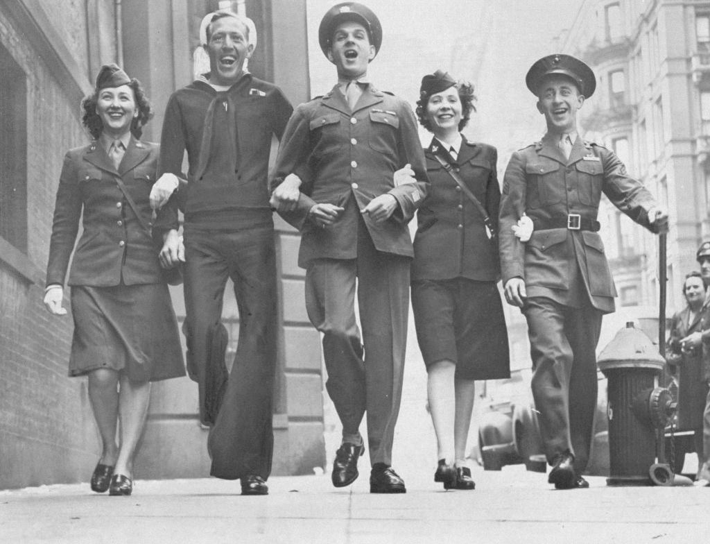 UNITED STATES - MAY 08: On V-E Day, members of the armed services stage an impromptu parade in front of City Defense Recreation Committee headquarters. Celebrating the allied victory in Europe are (l. to r.), WAC Pvt. Emily Struczewski; sailor Virgil Twilley; Army Sgt. Melvin V. Andrews; WAVE Veronica Van Kirk and Marine Sgt. Zigmund Gasiewics. (Photo by Charles Hoff/NY Daily News Archive via Getty Images)