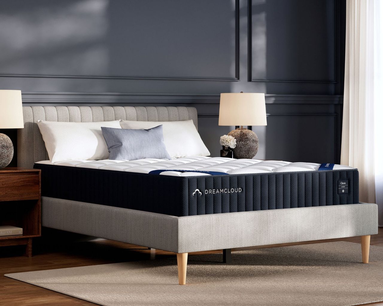 DreamCloud Classic Hybrid Mattress on a fluted bed in a black panelled bedroom with dark wood flooring with matching lamps to either side