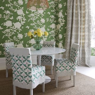 dining room with green floral wallpaper, round white table, white chairs with fabric, and neutral print curtains