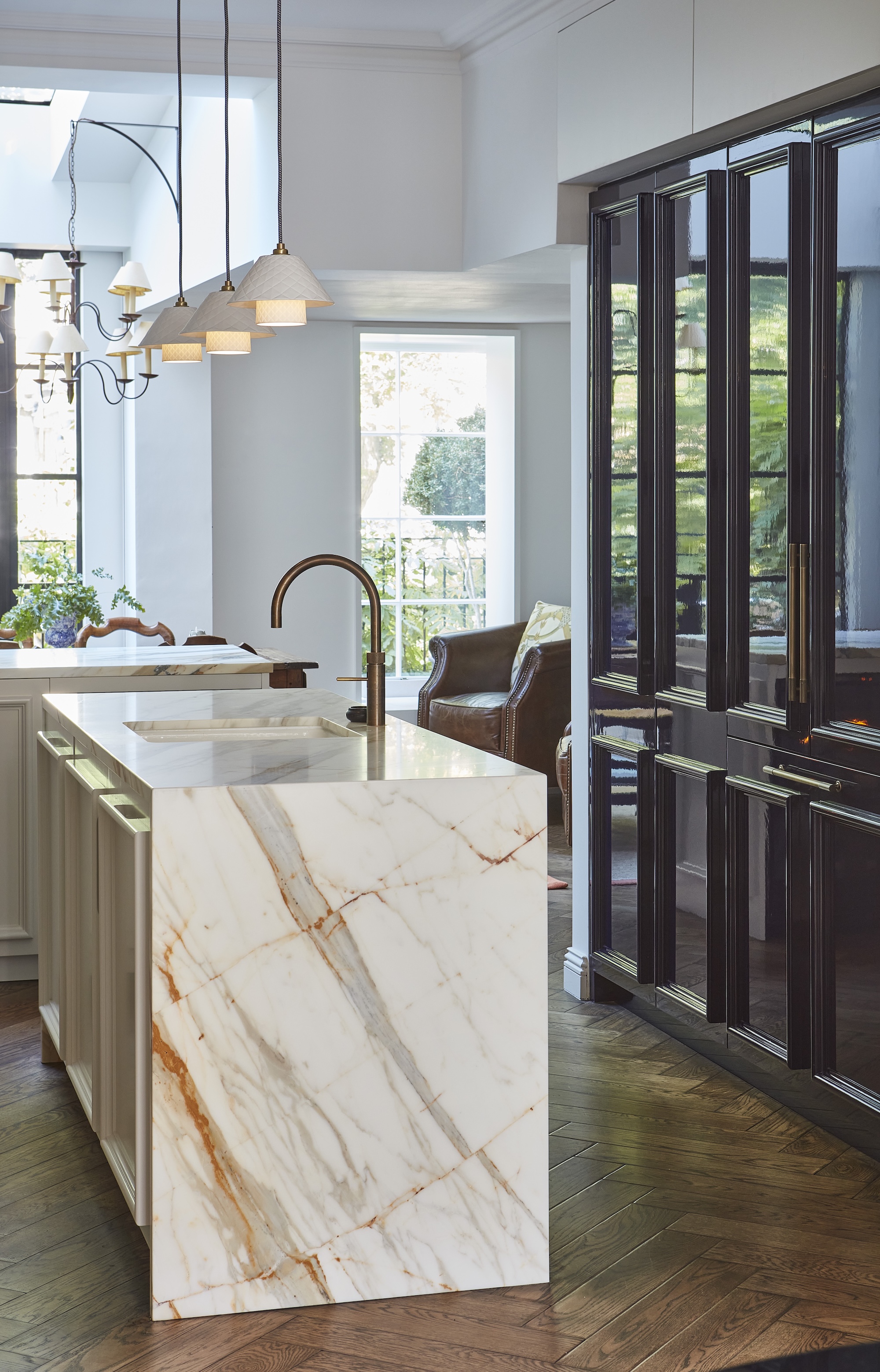 A light marble kitchen island opposite a run of tall, dark yet reflective cabinetry