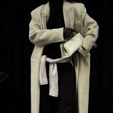 Person wears black turtleneck, cream long coat, cream handbag, black leather gloves