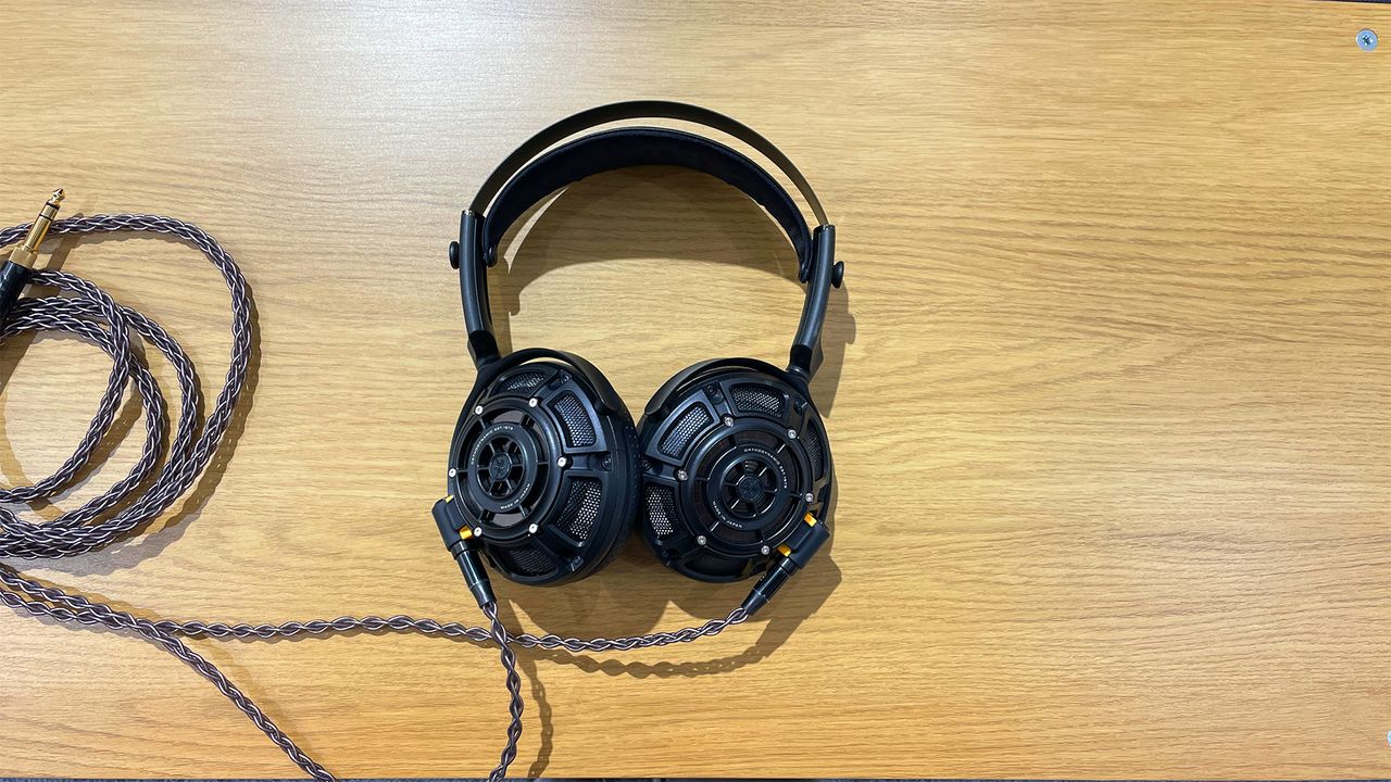 The Yamaha YH-5000SE over-ear headphones lying on a wooden surface, seen straight-on. The cable is rolled up next to the headphones.