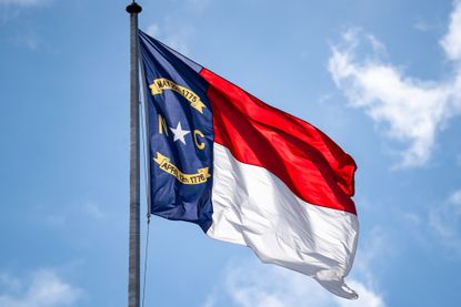 Close-up photo of a North Carolina state flag waving in the wind against a blue sky