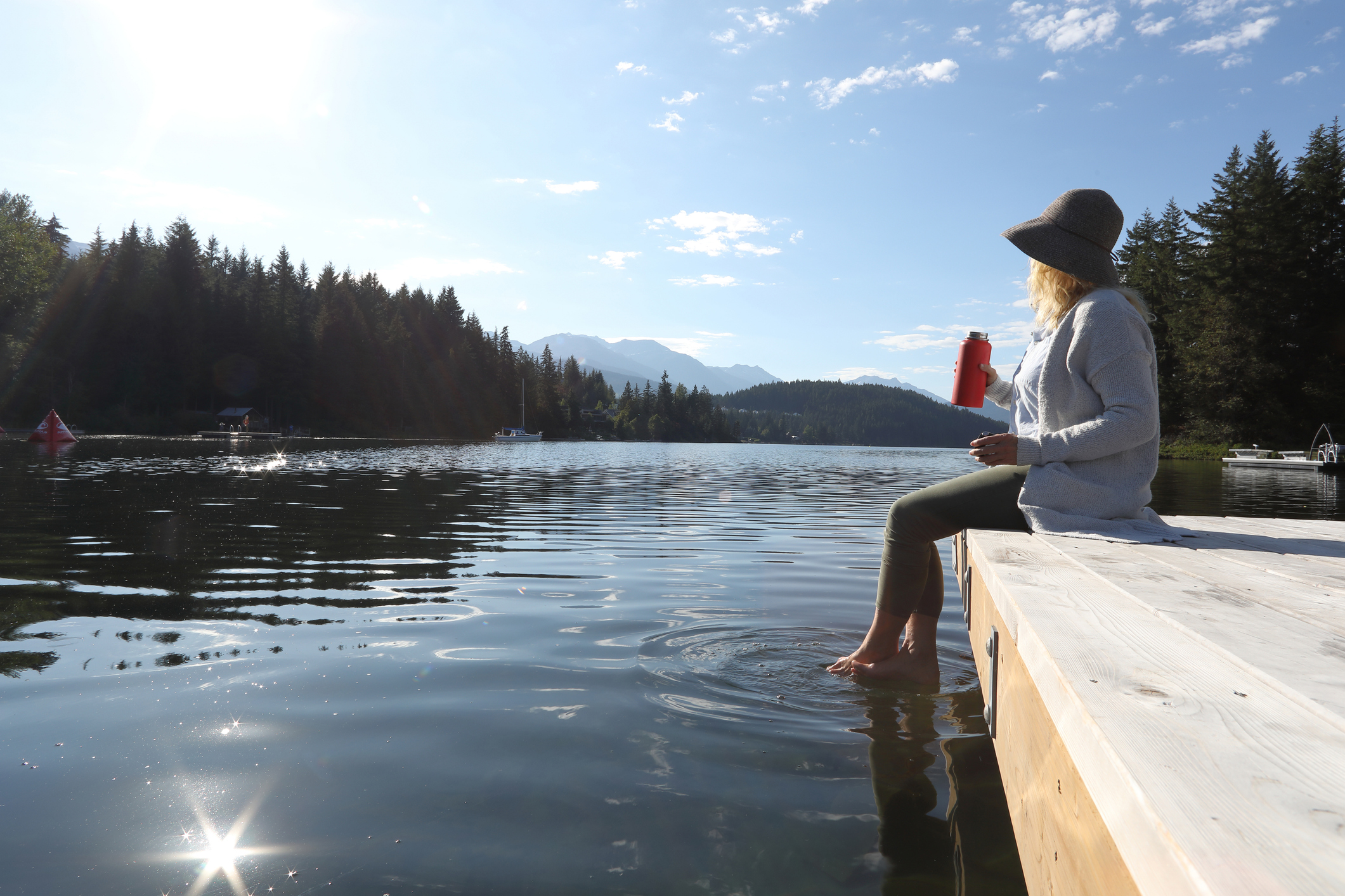 Woman dangles feet in a mountain lake at sunrise.