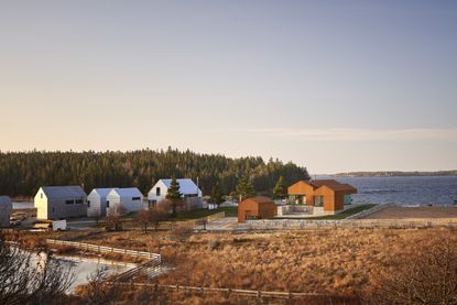 View of Smith House during the day which is made up of three Corten steel and stone pavilion structures. There are other houses nearby along with bodies of water and brown grassy land