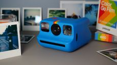 The Polaroid Go (Gen 2) on a grey background with images surrounding it