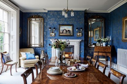 Dining room with long polished wood table with blue patterned wallpaper and Georgian sash windows