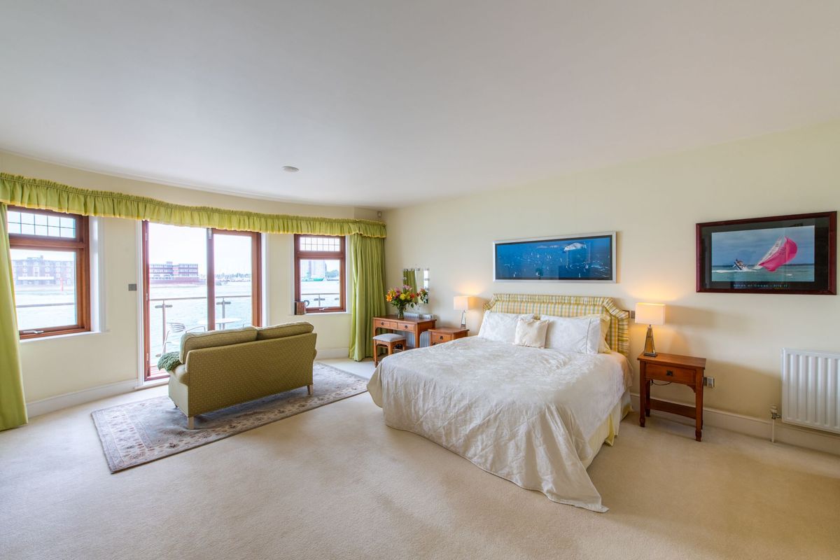 The master bedrooms has white linen sheets and a chair in the room faces the bifold doors which lead to the balcony overlooking the sea