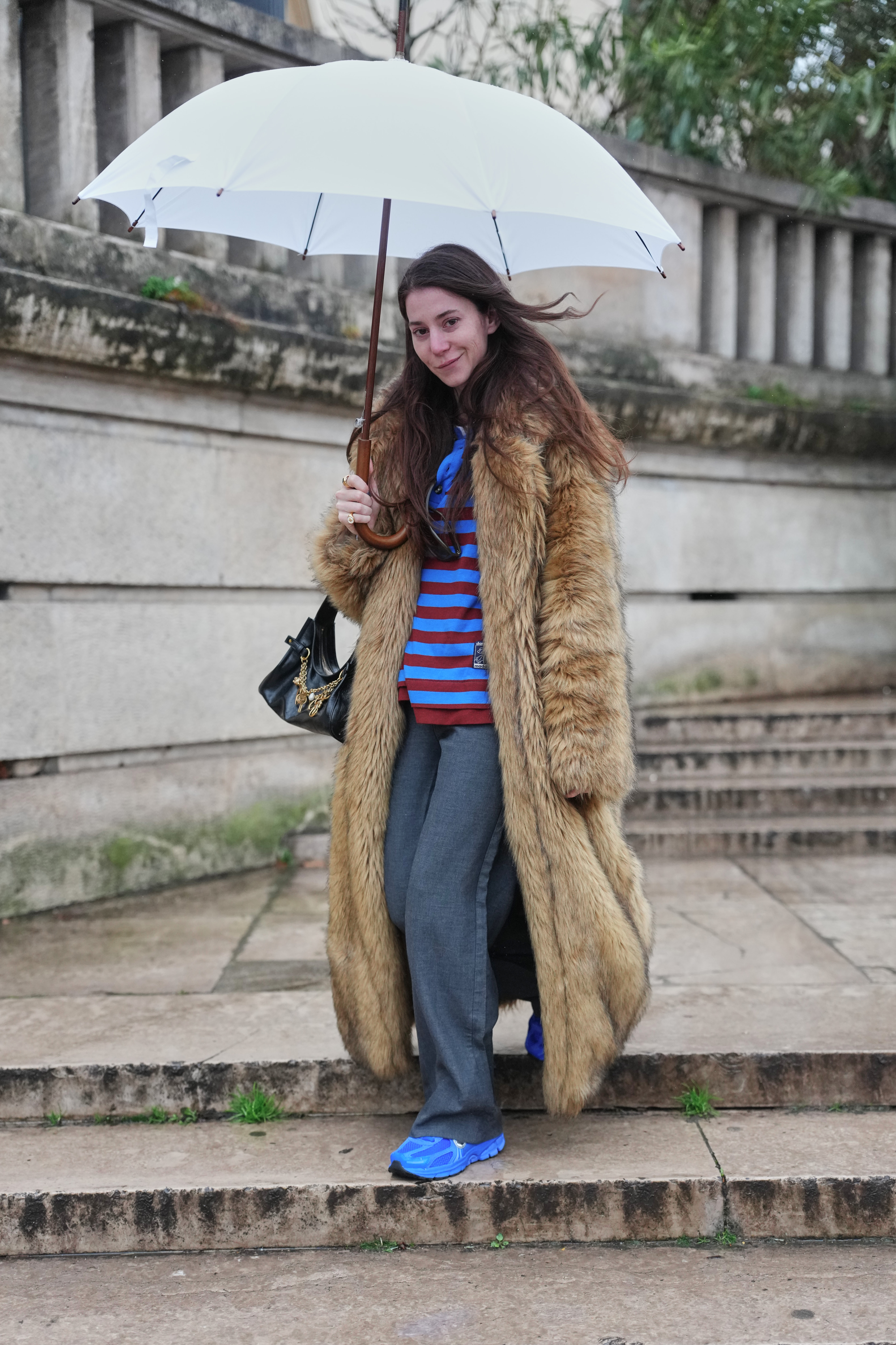 A guest wears a brown tan fur coat, a blue polo shirt with red stripes, gray wide jeans, and blue sneakers during Paris Fashion Week - Menswear Fall/Winter 2026 on January 25, 2026, in Paris, France.