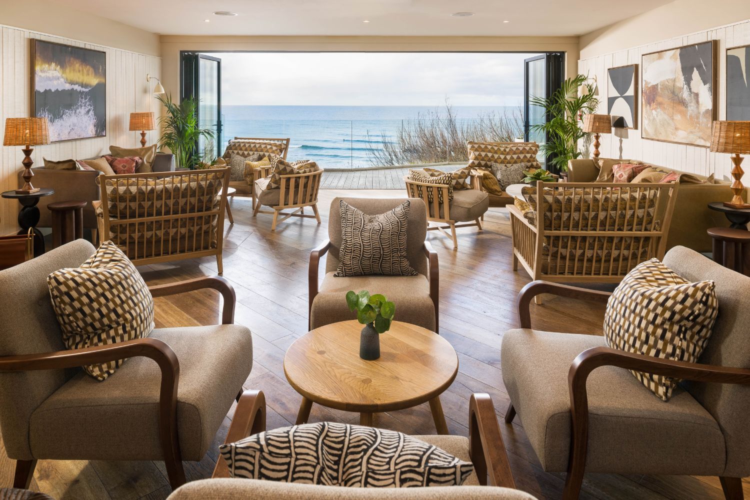image of a bedroom at Watergate Bay, chairs and tables lead to glass doors that open to a view of the blue sea