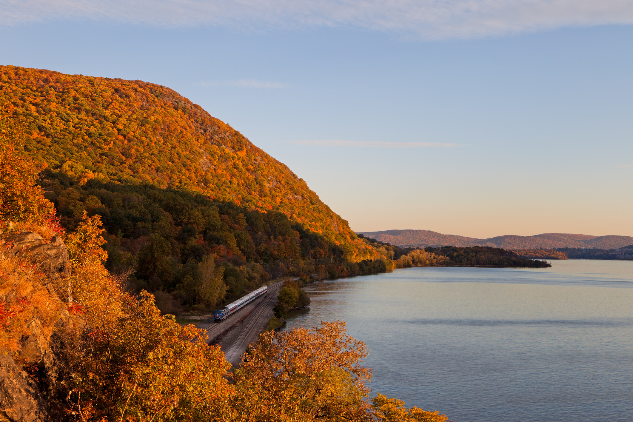 Fall foliage surrounding a NYC commuter train at sunset along the Hudson River near Cold Spring, NY.
