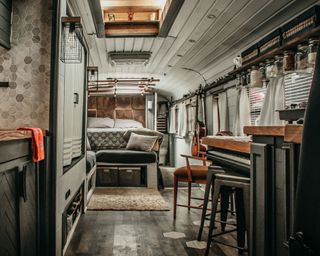 interior of Caleb's converted bus, with black kitchen units and wooden tops, a gray bed in the background, and gray walls and gray curtains