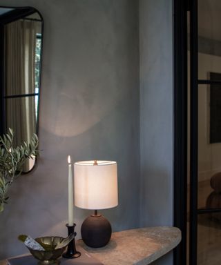 a white and black lamp on a stone side table, in a blue room, next to a wall mirror with a black rim