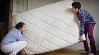 How to choose a mattress for your preferred sleep position: a young couple move a new mattress into their bedroom