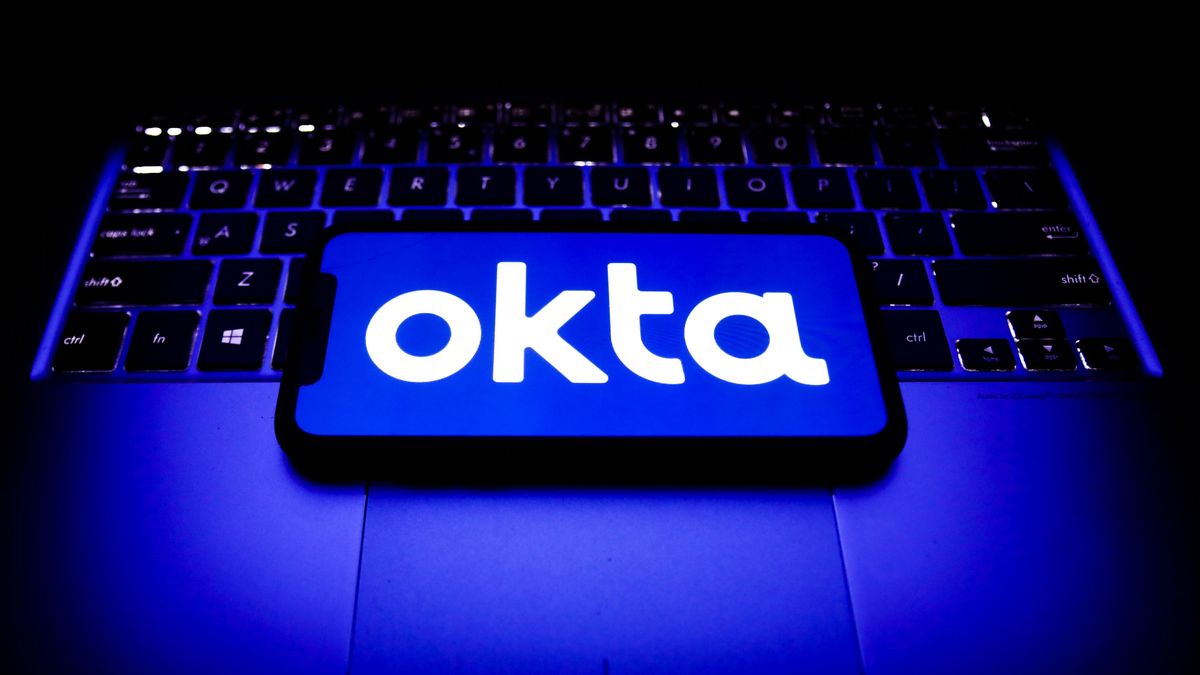 Okta company logo appearing on a smartphone which is placed upon a Windows laptop&amp;#039;s keyboard