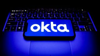 Okta company logo appearing on a smartphone which is placed upon a Windows laptop&amp;#039;s keyboard