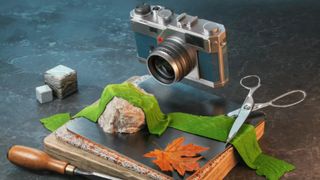 Image of 3D designed products includiong, a camera, scissors, a green ribbon, a chisel in wood, some cubes, some mats, and a rock