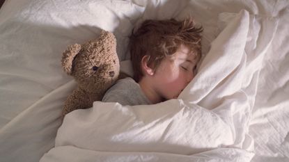 A boy sleeping in his bed with his teddy bear
