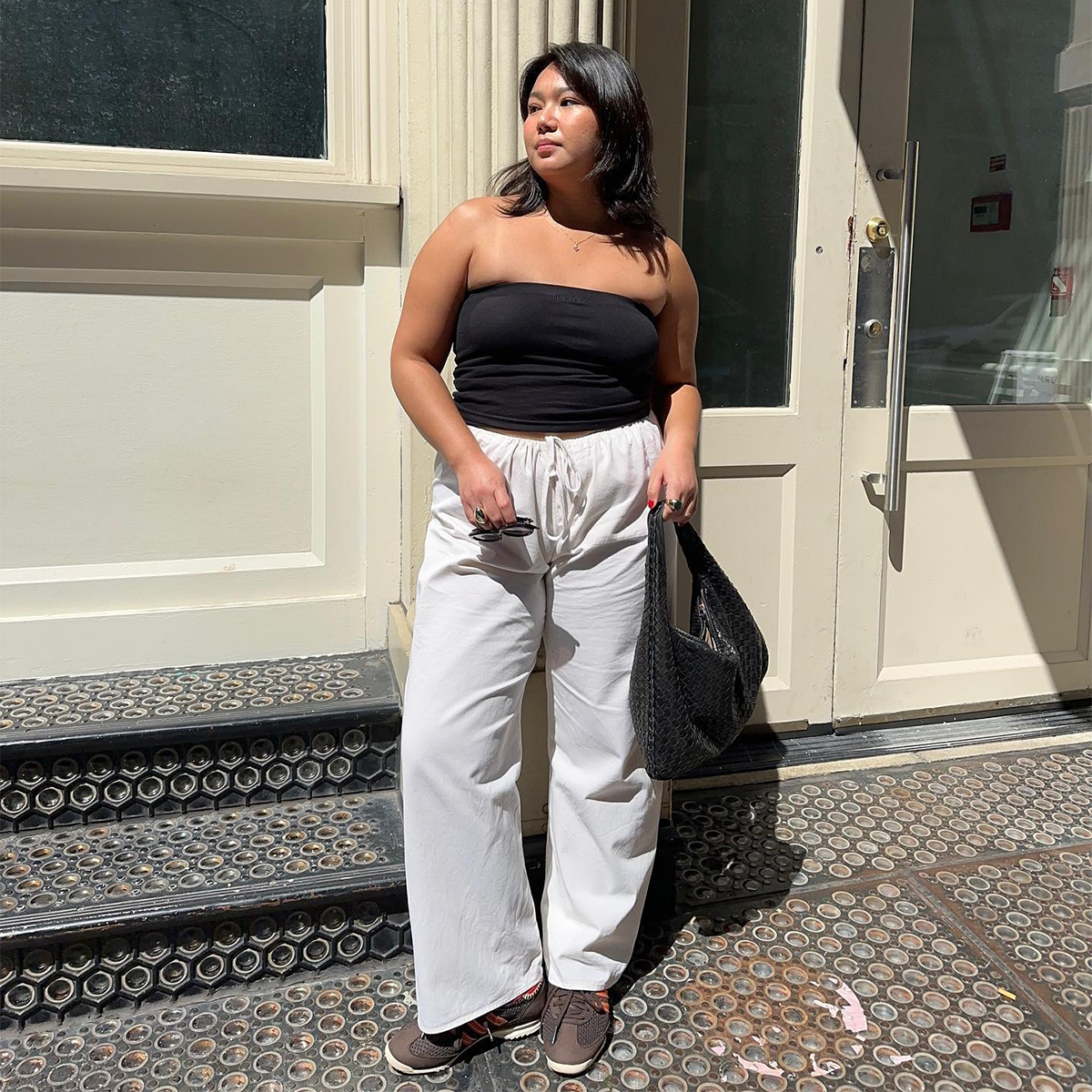 Influencer Marina Torres wears white linen trouser, a black tube top, and a woven black hobo bag. 