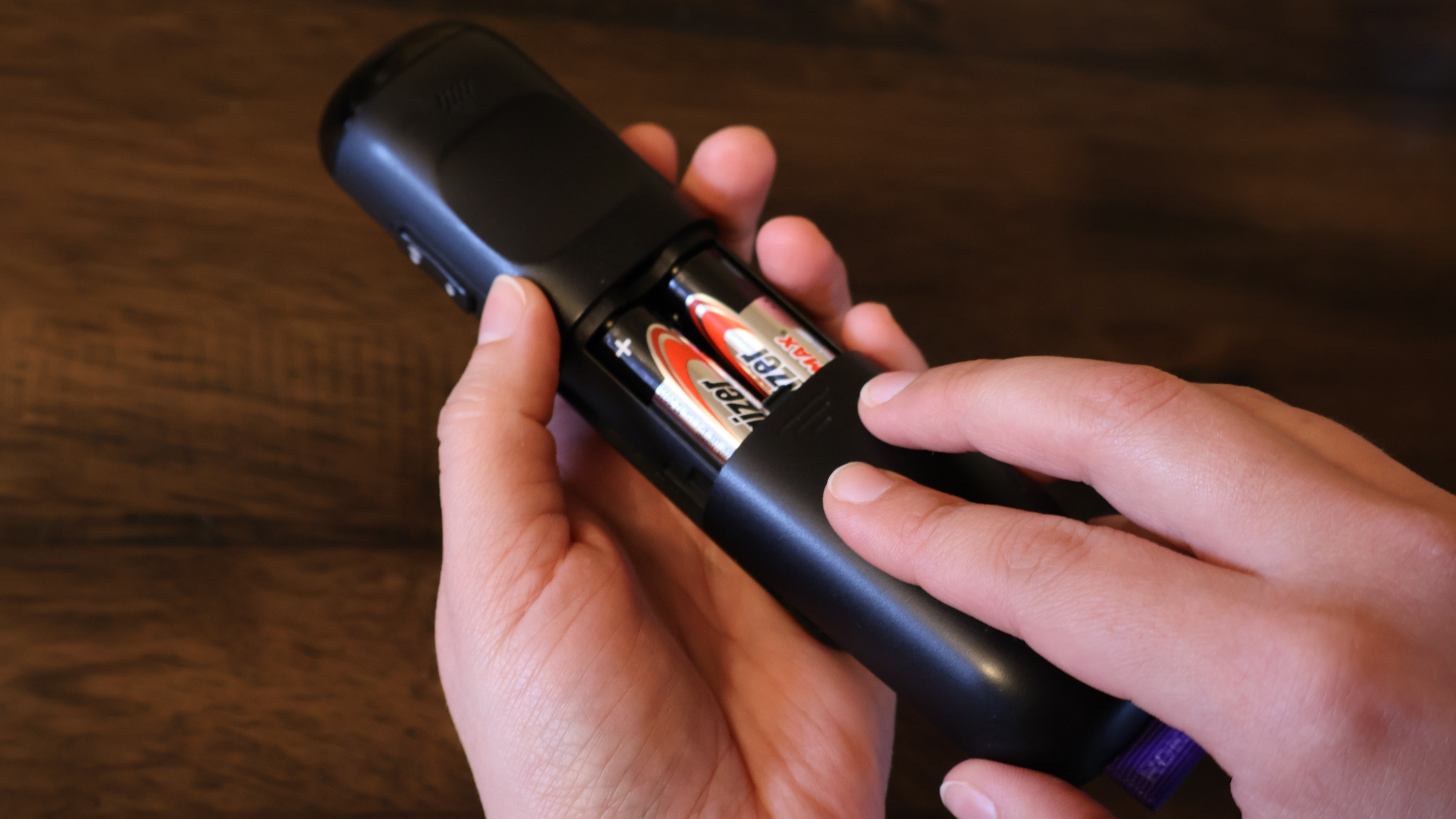 A pair of hands sliding the battery cover closed on a TV remote containing two AA-sized batteries