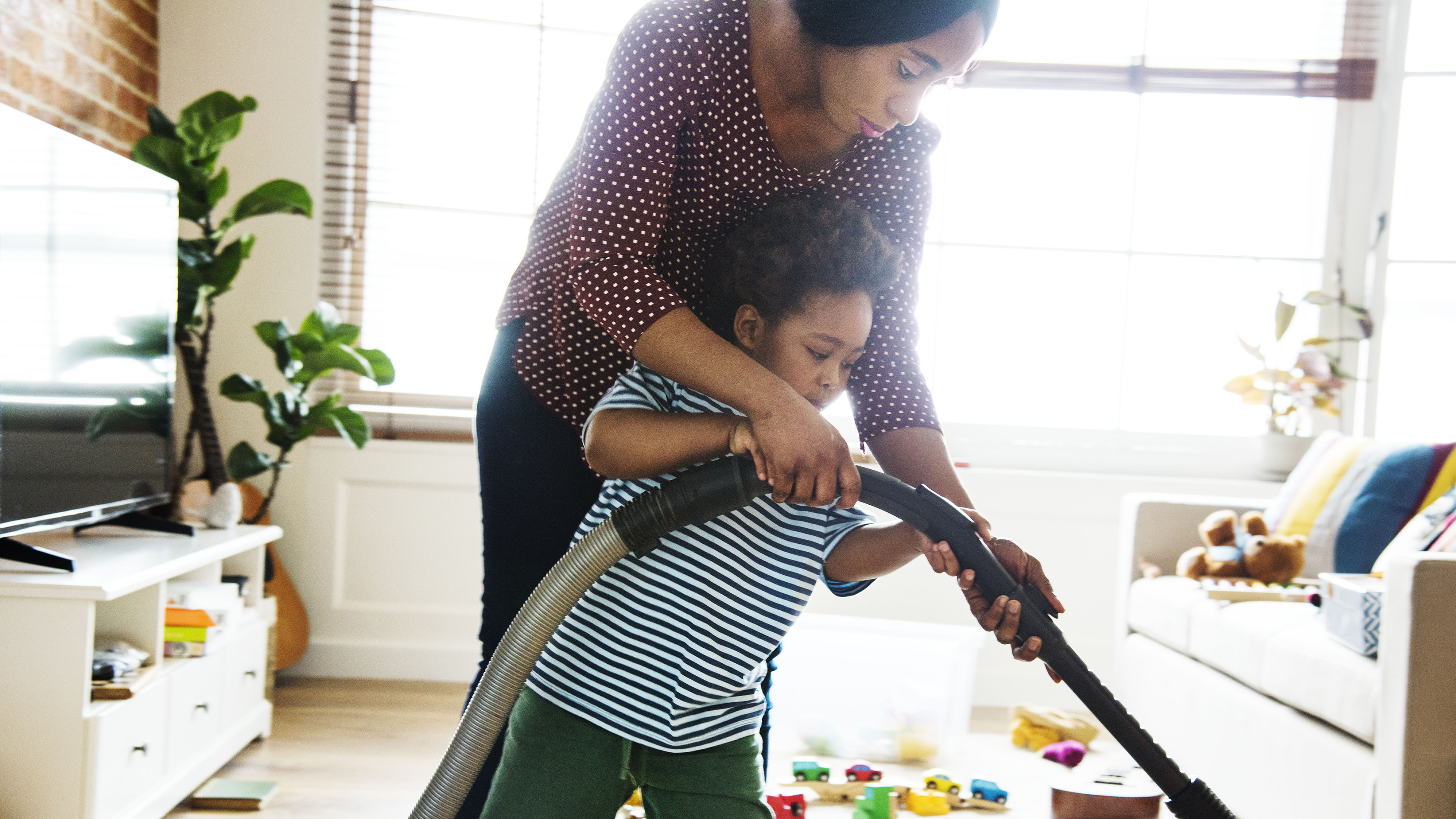 Woman hoovering room with little boy