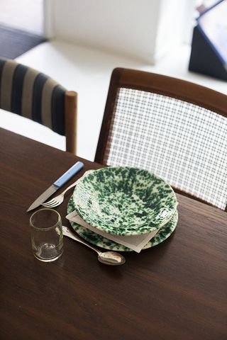 A close up of a table setting on a dark wooden table, with white and green marbled plates, silver cutlery and one glass