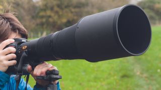 A person looking through an ultra zoom lens, which is mounted on a tripod