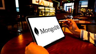 MongoDB logo and branding pictured on a handheld tablet device by man sitting in coffee shop.