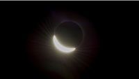 The moon's disk is pictured hiding the upper left portion of the sun in a darkened sky during an eclipse.