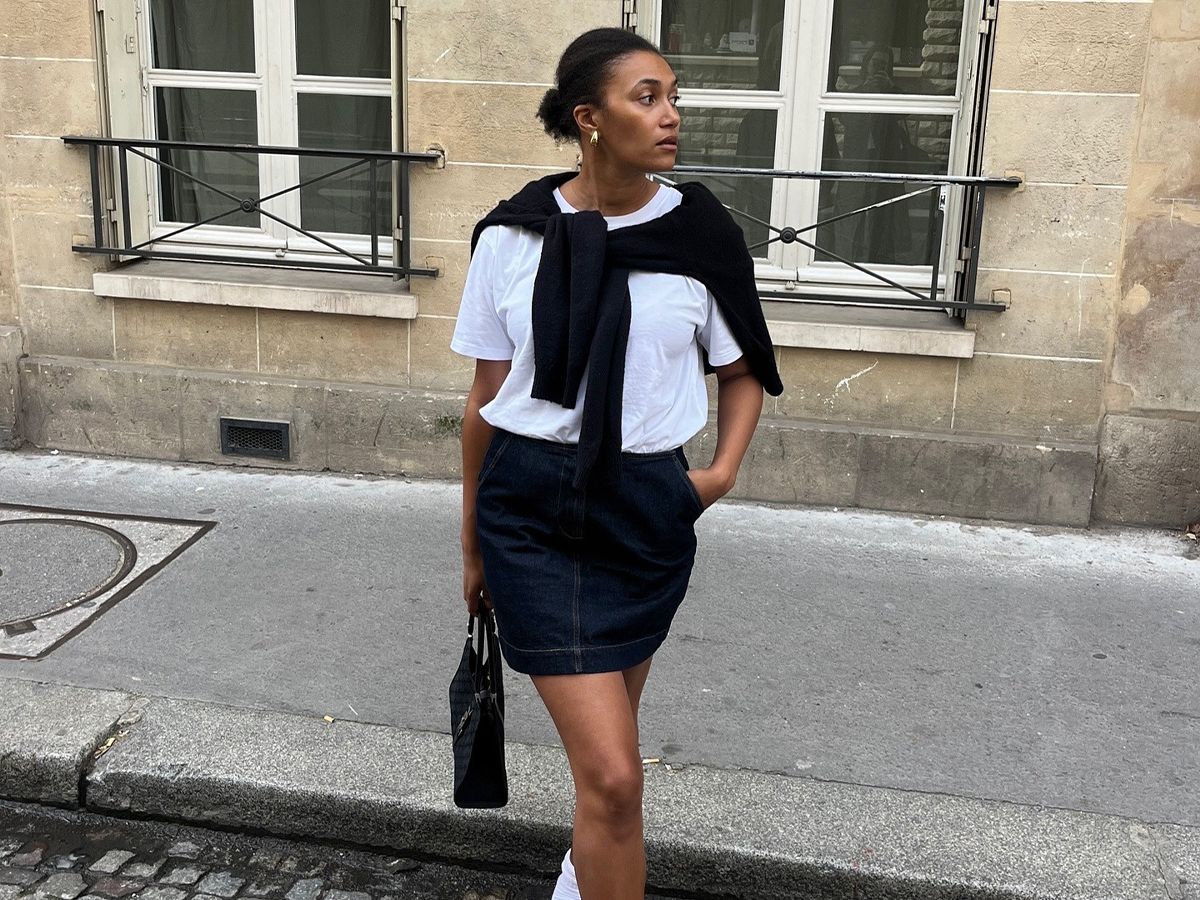 Influencer Lena Farl wears a denim mini skirt and a white crewneck with white socks and black ballet flats.