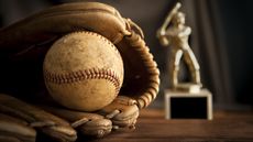 An old baseball glove and ball and baseball trophy sit on a desk.