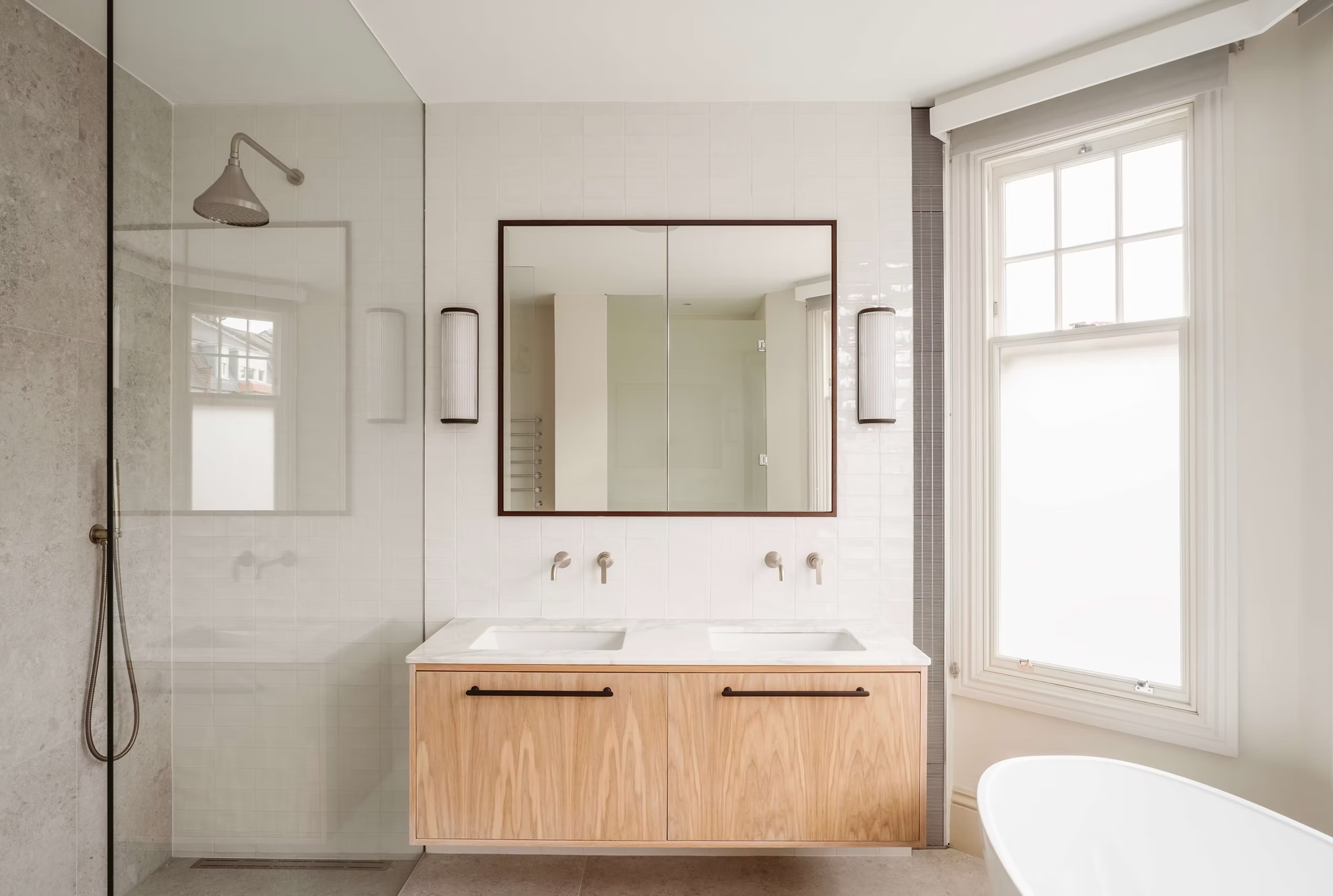 A contemporary bathroom with window film, a floating timber vanity with double sinks and black hardware, silver taps, a shower screen and rainfall shower, shaving cabinet with sconces on either side