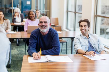 A mixed age group laughs as the teacher uses humor to introduce the resume writing class.