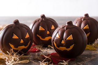 four chocolate pumpkins on bits of hay and leaves sitting on a wooden surface