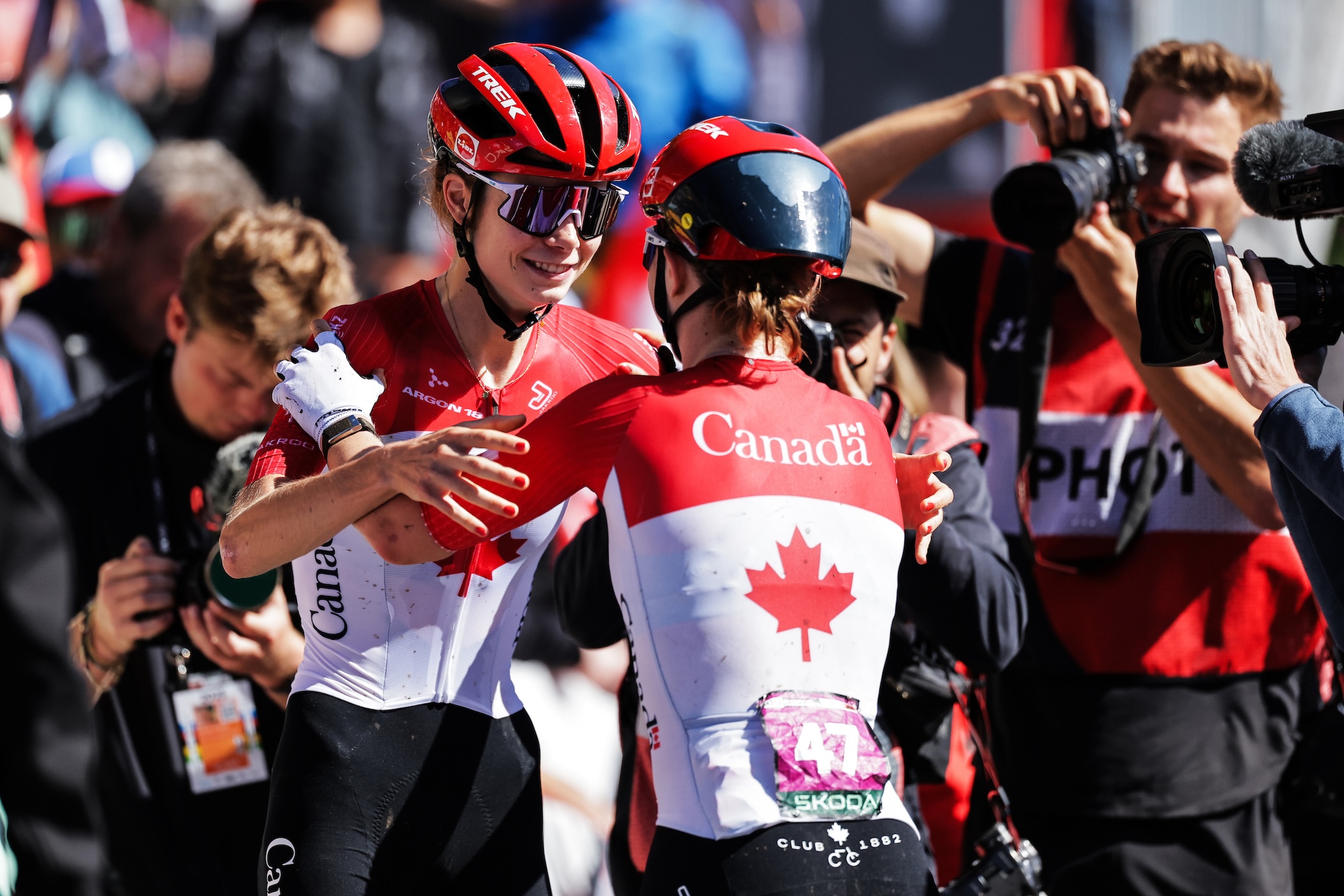 At the 2025 UCI Mountain Bike World Championships racing for Canada, Isabella Holmgren (on left) celebrates a win in U23 XCO race with a hug from sister Ava