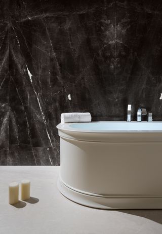 A dark stone surface forms the backdrop to a white minimalist bathtub