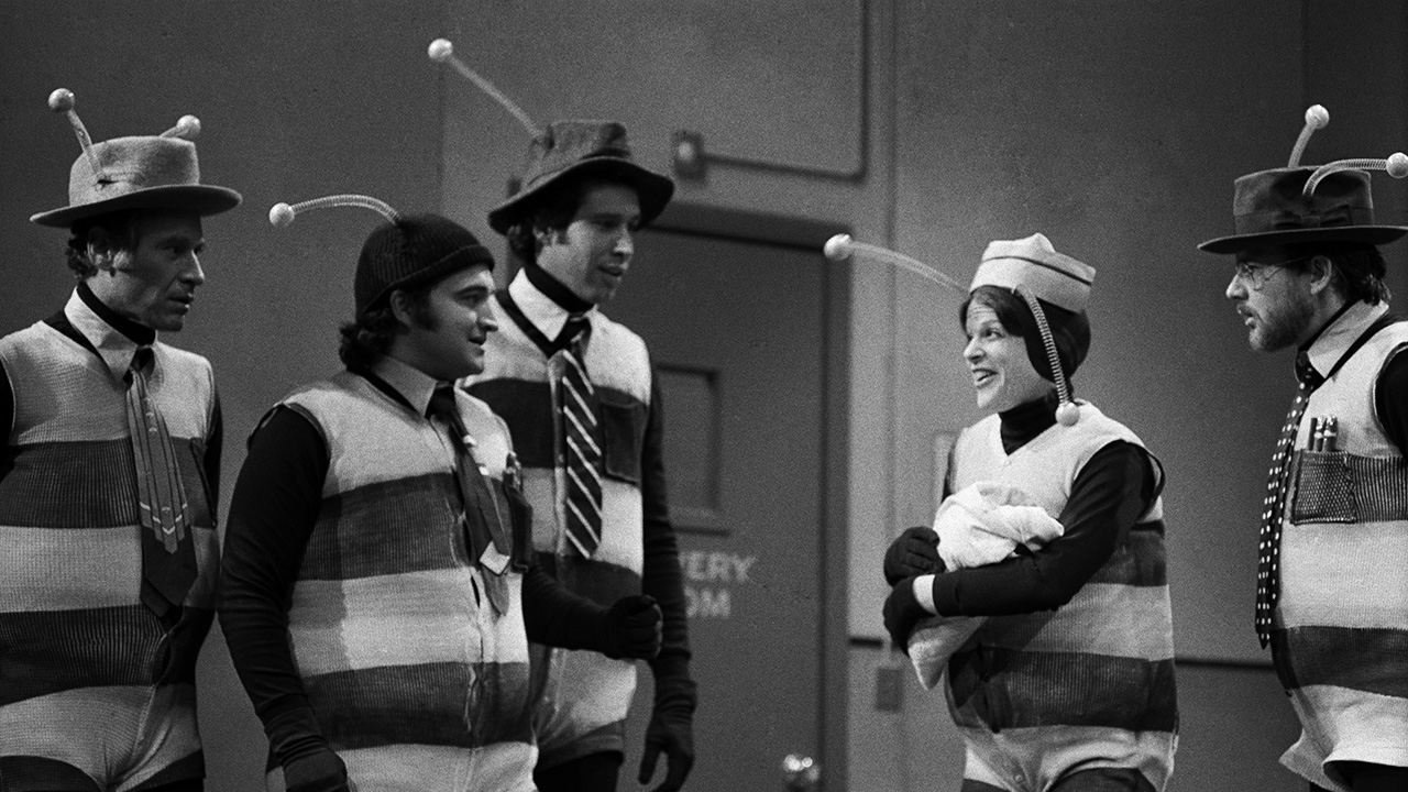 Black-and-white NBC image of Gilda Radner, Chevy Chase, John Belushi and co in the infamous SNL Bee suits from Season 1, 1975.