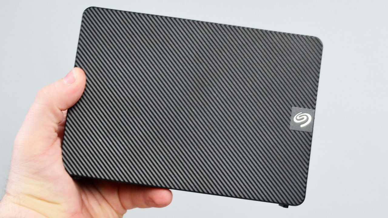 A masculine hand holding a Seagate Expansion external desktop hard drive