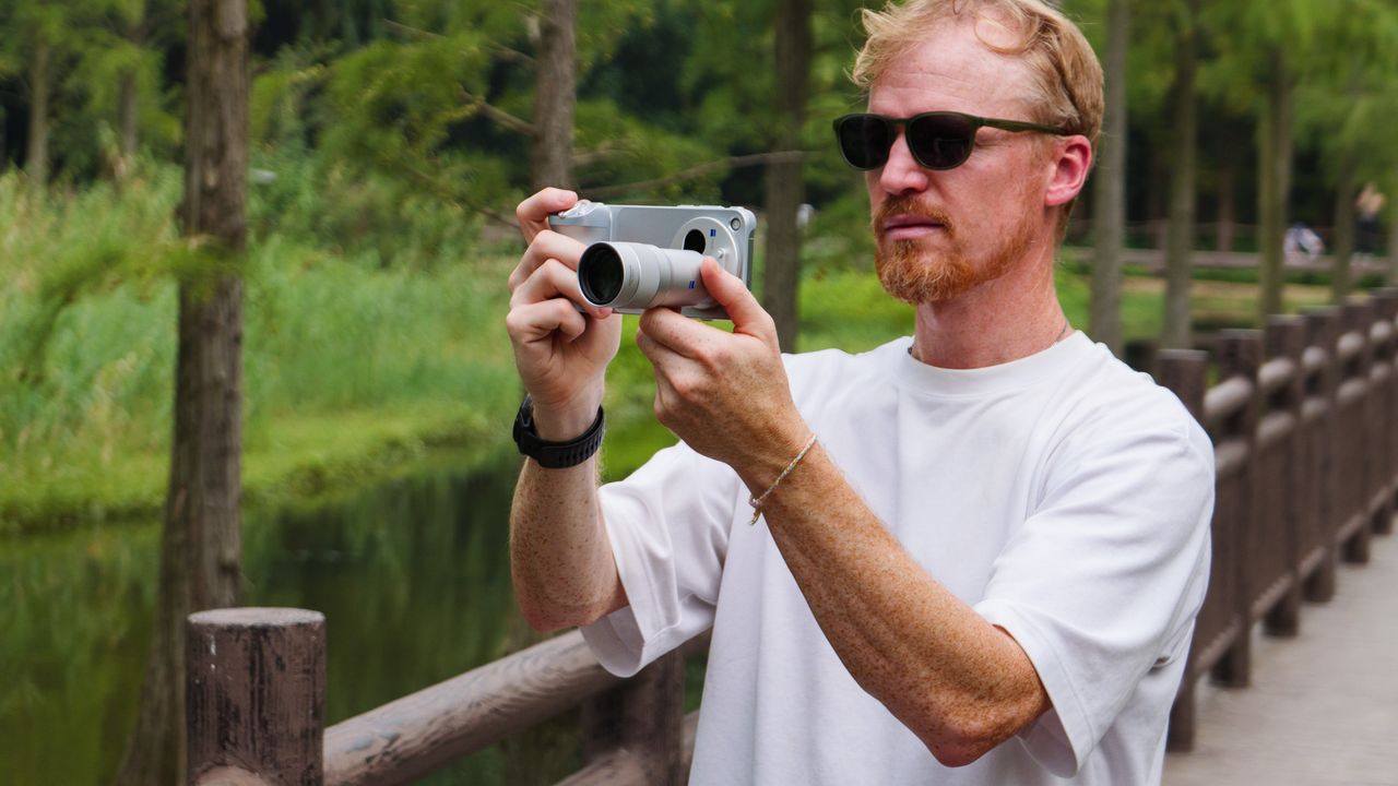 Tim Coleman, TechRadar's Cameras Editor, holding the Vivo X500 Pro Max phone with teleconverter lens attached, while stood on a wooden walkway in a birdlife reserve in Shanghai, China