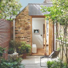 Brick wall exterior of extension to 3 storey inner-city Georgian house from garden with stone paving and shrubs Refurbished three storey, three bedroom inner city Georgian house, home of Harriet Paterson and Warren Bramley