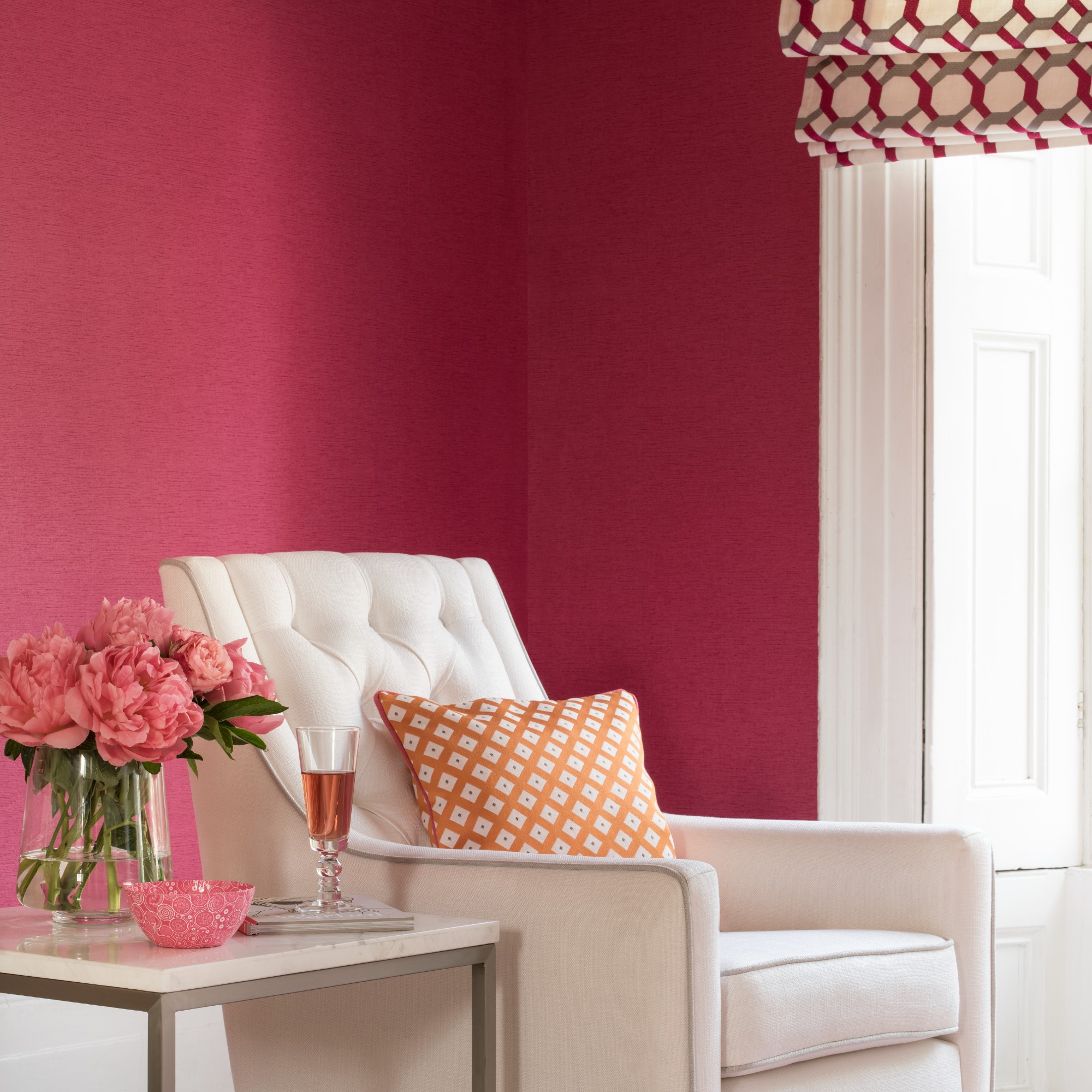A living room with bold red walls with a pink undertone and a cream armchair