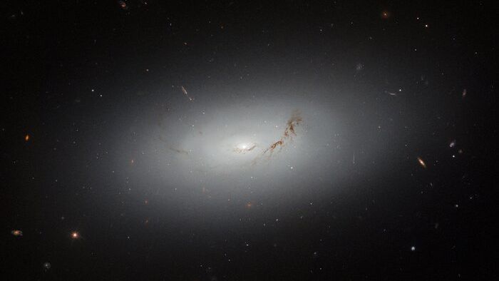 a glowing with galaxy hangs center amongst small, distant dots, which are also galaxies.