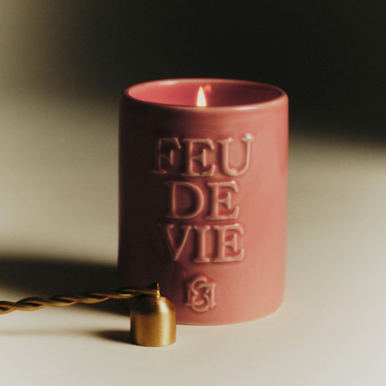 A candle in an orange ceramic jar by a snuffer