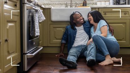 Romantic couple sitting on the kitchen floor, arms wrapped around each other, representing the cowgirl's helper sex position