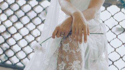 A bride in a delicate lacy wedding dress, holding a white flower and wearing a simple French manicure