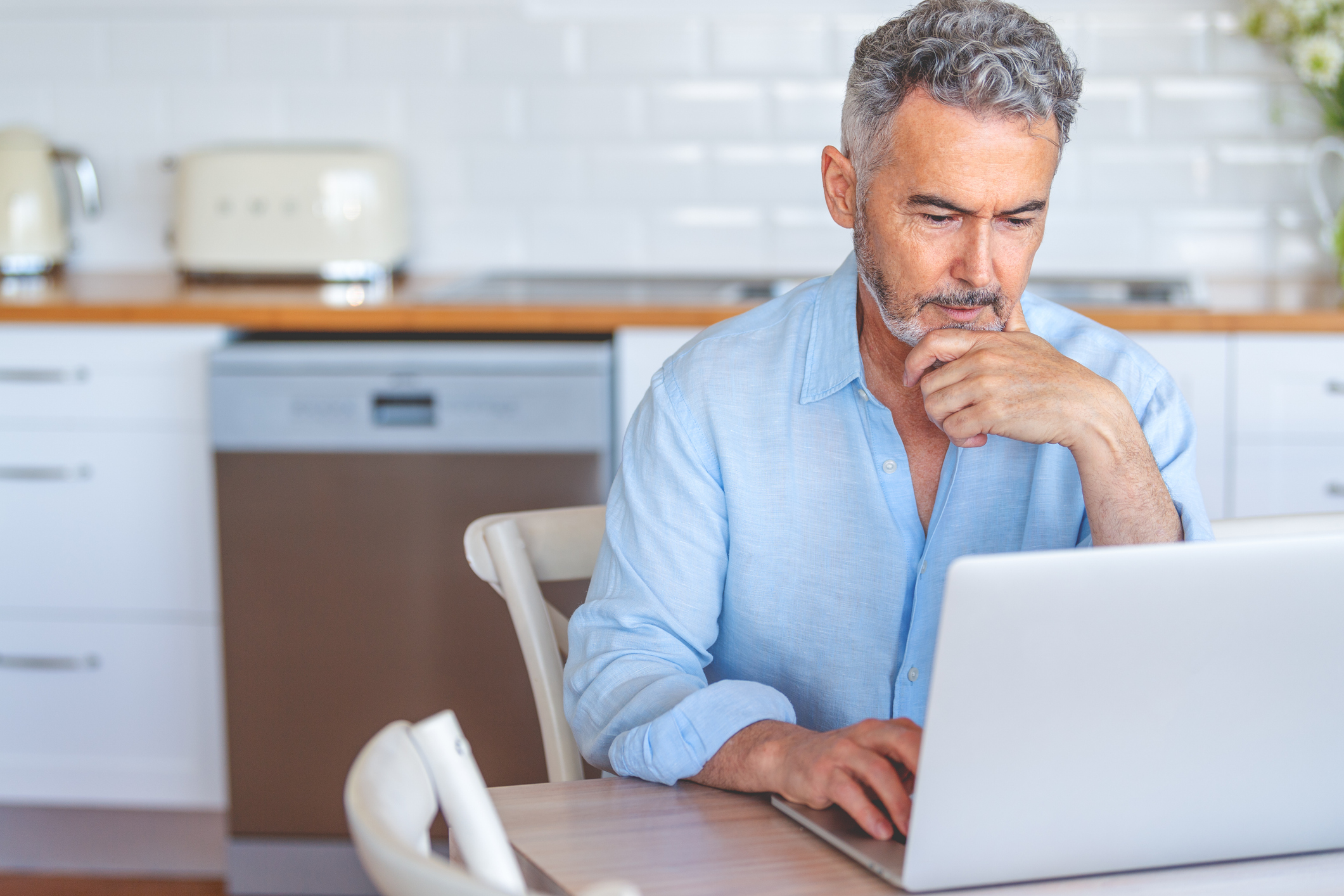Mature businessman working on a laptop at home. He is concentrating and casually dressed.
