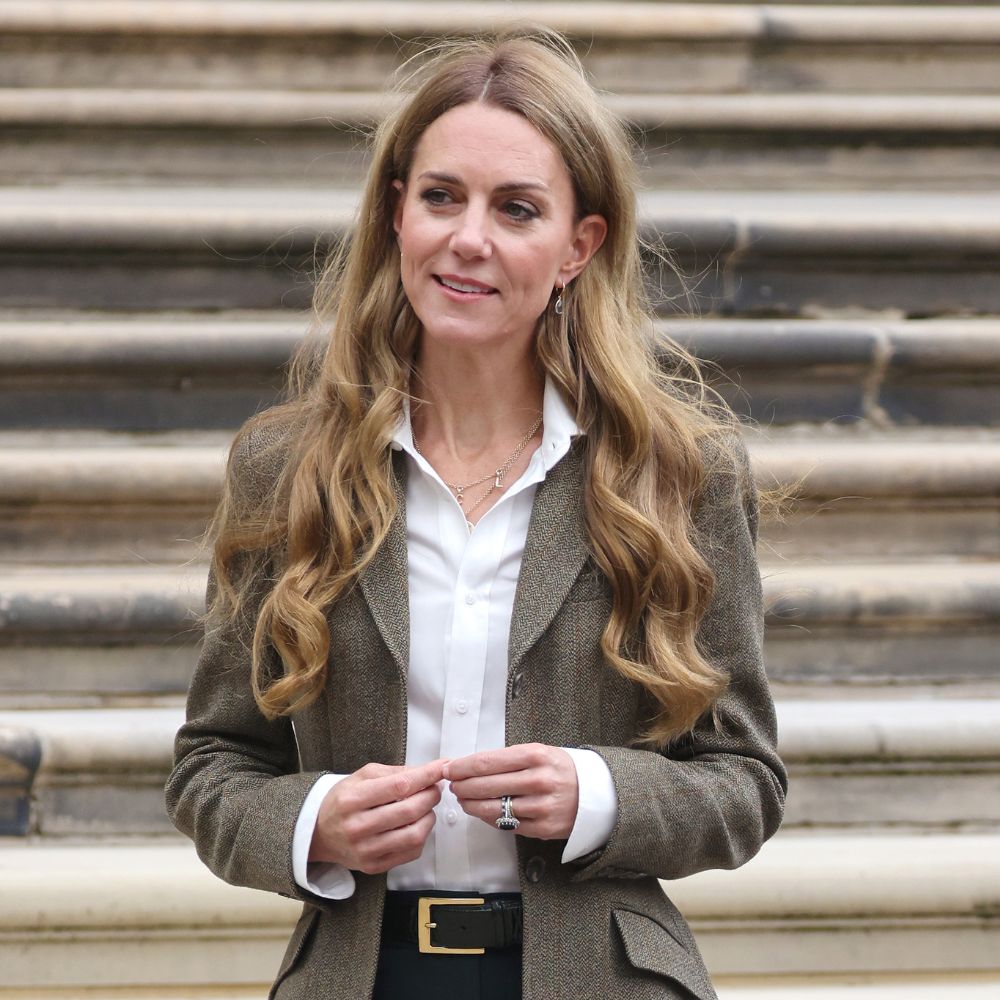 Kate Middleton walks outside wears a tailored blazer, white shirt, dark green jeans and suede loafers.