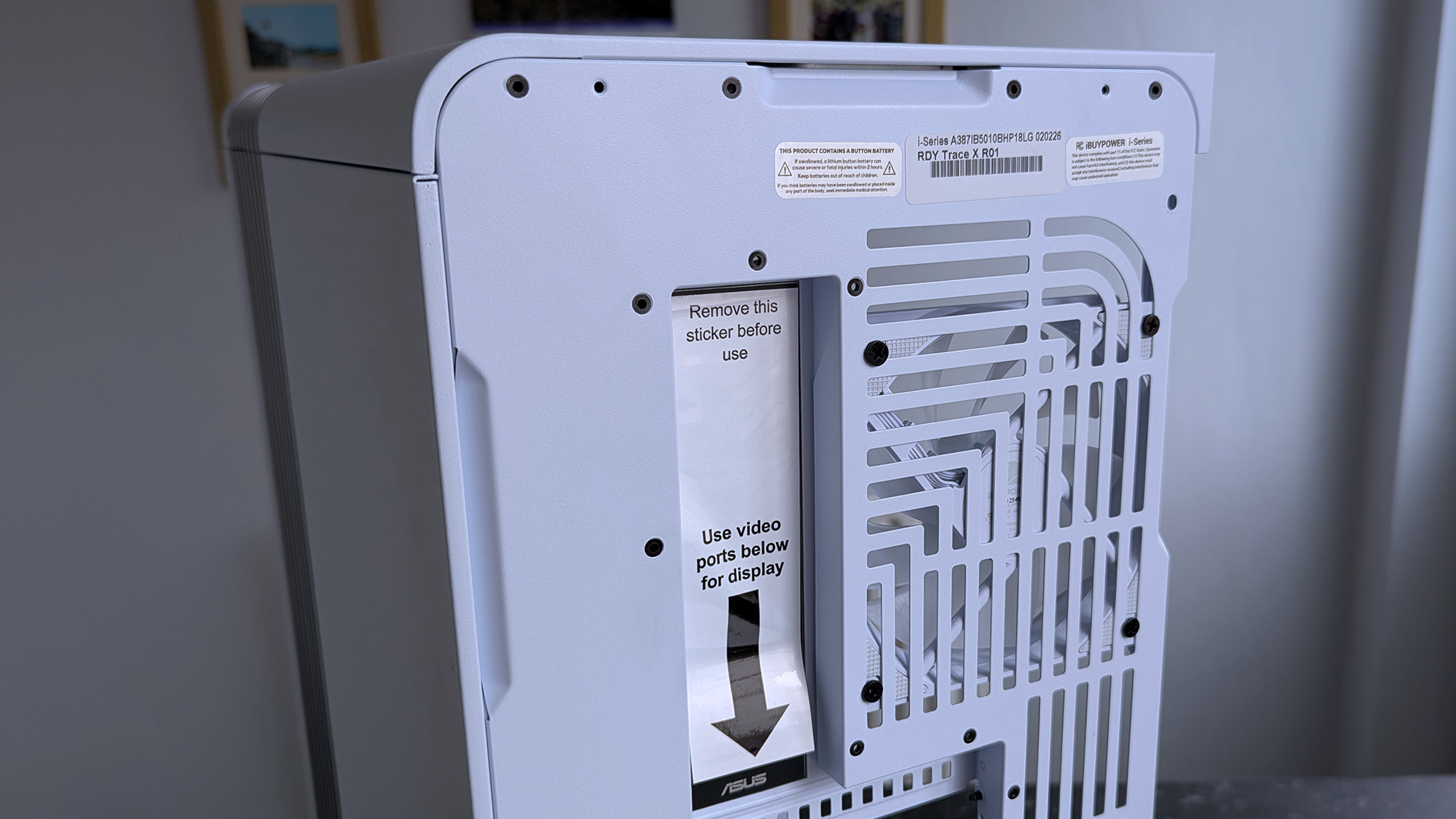 The back of a white iBUYPOWER RDY Trace X R01 computer with vented slots and a shiny sticker that reads, "Remove this sticker before use."