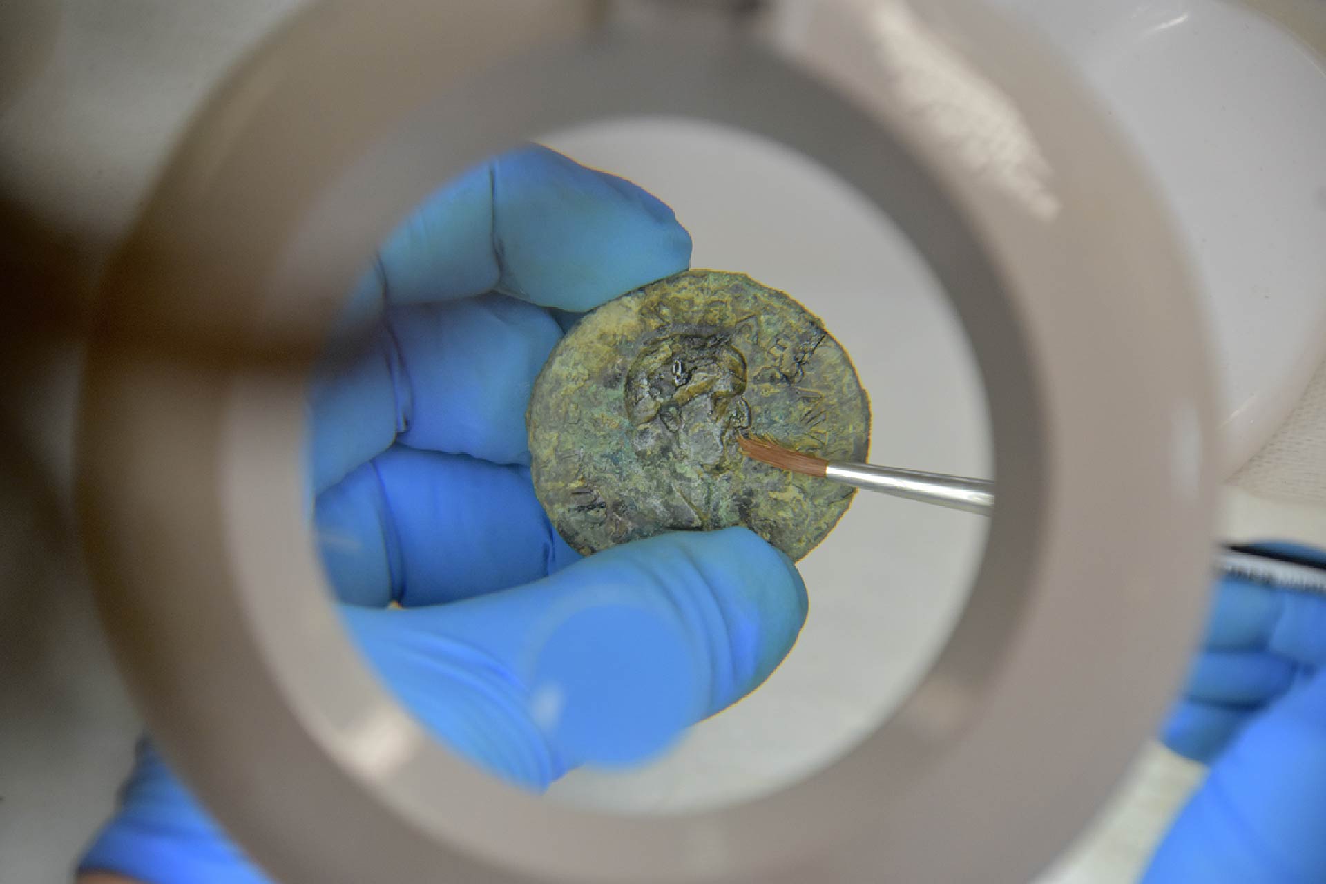 Close-up look of an archaeologist holding onto a gold coin using a glove