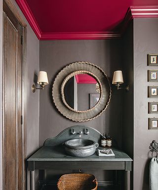 Dark grey walls and vanity unit, round mirror and a plum coloured decorated ceiling.